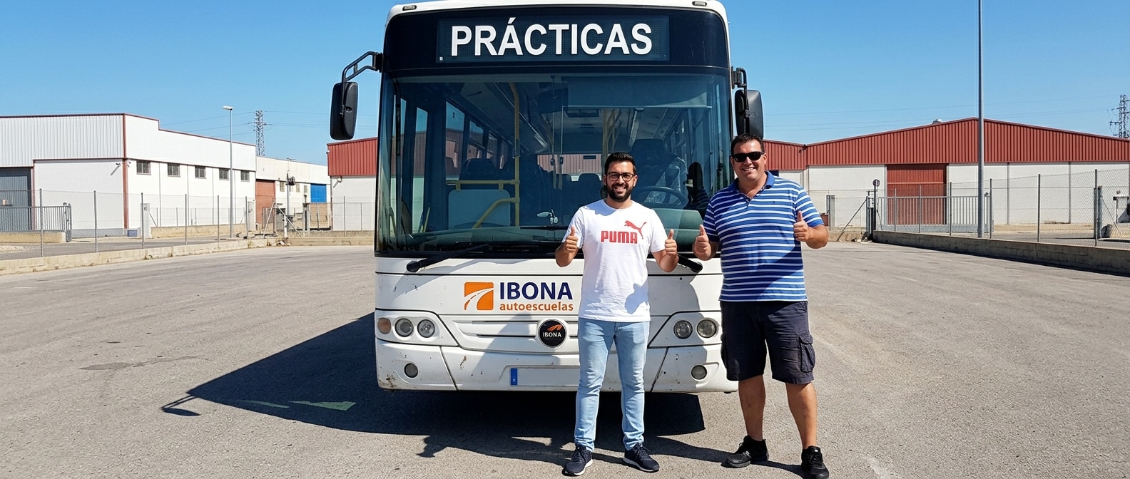 Dos hombres posan con los pulgares levantados delante de un autobús de prácticas de autoescuela, relacionado con la formación para obtener el carnet D de autobús.